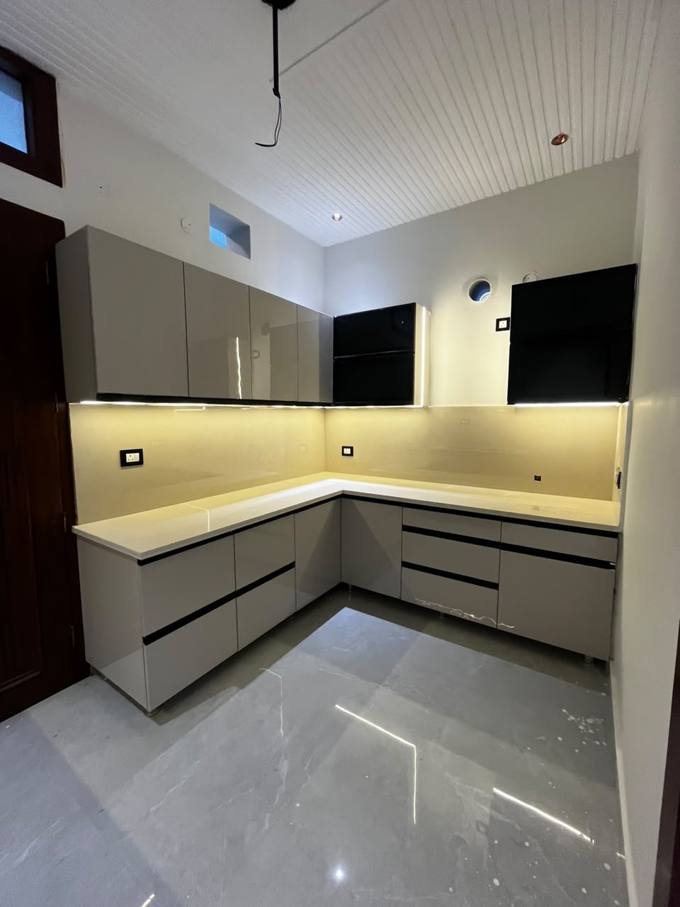 Glossy grey L-shaped modular kitchen with under-cabinet lighting